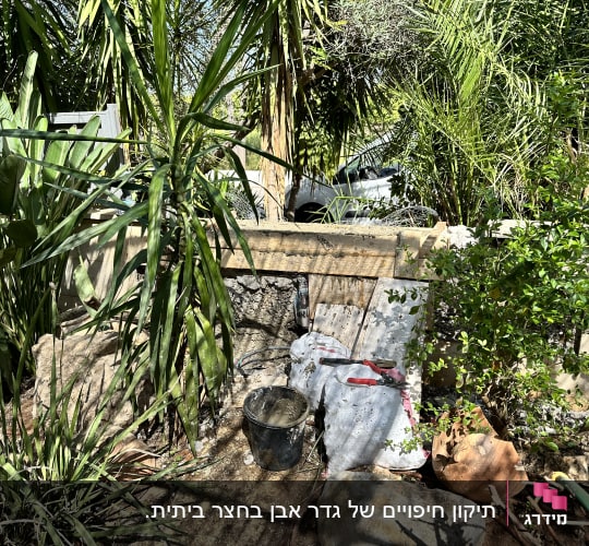 דלי, שק מלט וכלי עבודה ליד קיר בטון